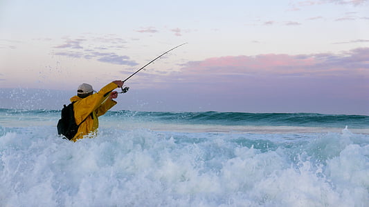 man wearing orange windbreaker jacket holding telescopic fishing rod on sea water thumbnail