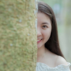 Woman in White Off-shoulder Top Behind Grey Tree Trunk thumbnail