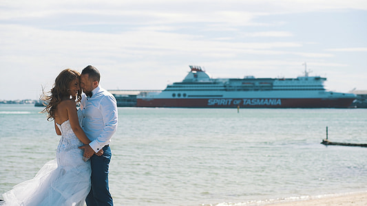 man and woman in wedding clothes overlooking boat on sea thumbnail