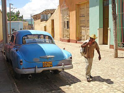 man walking near parked blue car and buildings thumbnail