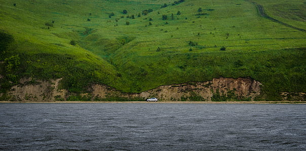 silver vehicle on road near body of water and mountain thumbnail