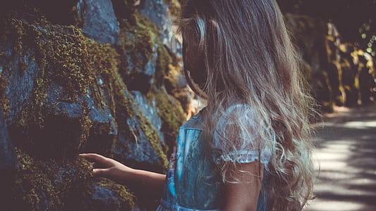 girl touching green moss on gray rocks at daytime thumbnail