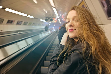 Young Blonde Woman In Black Leather Jacket Looking Over Shoulder While Using Escalator thumbnail