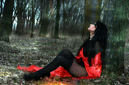 woman wearing red and black mesh bodysuit sitting beside tree thumbnail