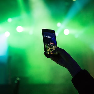 selective focus photography of person holding smartphone turned-on taking photo of crowd at concert thumbnail