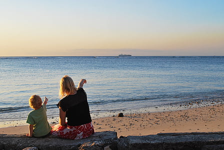 woman beside toddler sitting on concrete while pointing on beach thumbnail
