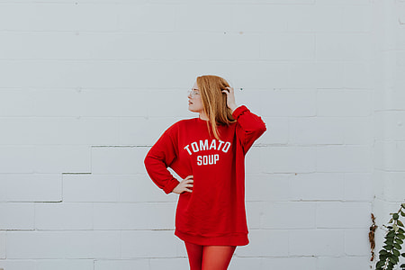 woman in red Tomato soup printed jacket standing near white concrete wall with green leafy plant thumbnail