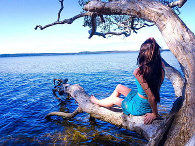woman sitting on brown tree branch near body of water thumbnail