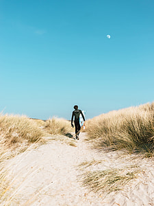 man wearing black wet suit walking on sand thumbnail