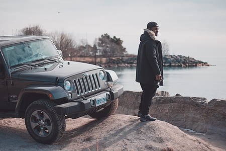 man standing beside black Jeep Wrangler SUV near body of water thumbnail
