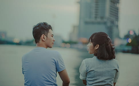 Man and Woman Facing Body of Water and Building thumbnail