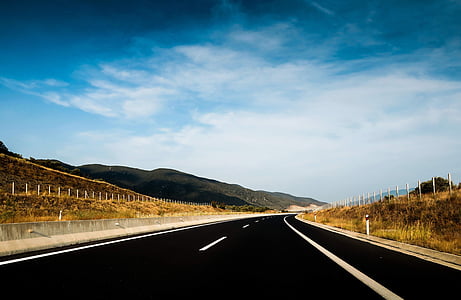 black road between brown grass-covered fields under thin white clouds photo thumbnail