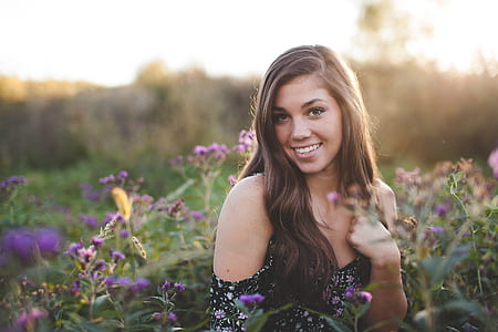 Woman in Black Off Shoulder Dress Standing in Green Flower Field during Daytime thumbnail