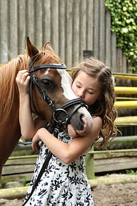 girl wearing white and black floral dress hugging brown horse head during daytime thumbnail