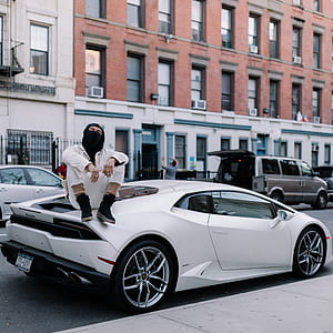 man wearing white top sitting on coupe near building thumbnail