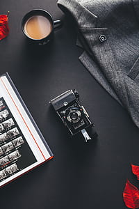 black ceramic mug with coffee inside beside gray suit jacket and black camera on table thumbnail