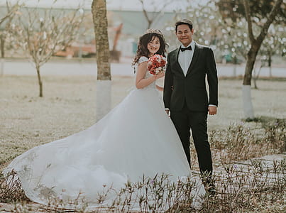 Woman Wearing White Wedding Ball Beside Man Wearing Black Notch-lapel Suit on Pathway Near the Green Grass Field thumbnail