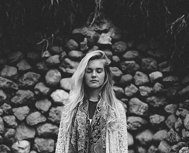 woman standing in front of piled rocks in grayscale photography thumbnail