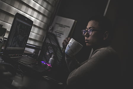 grayscale photography of man watching on laptop while holding mug thumbnail
