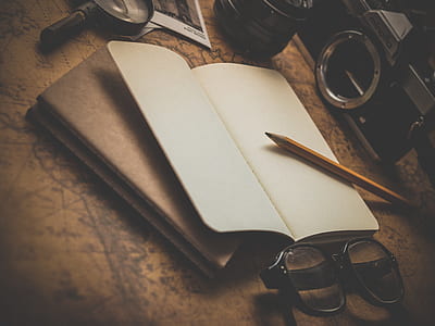pencil, black framed eyeglasses, book, camera, and magnifying glass on brown surface thumbnail