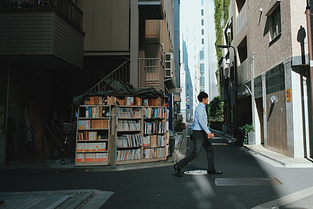 man walking near assorted book display lot outside concrete buildings thumbnail