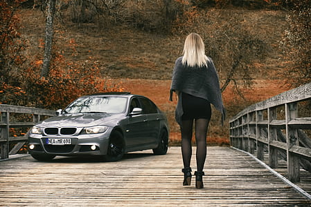 woman walking on bridge with gray BMW sedan in distant thumbnail