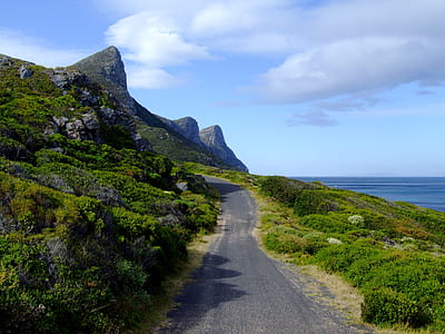 mountain pass beside ocean under white clouds thumbnail
