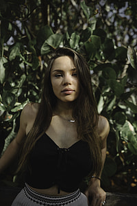 close up photo of woman with black strapless crop top leaning on brown wood in front green leaf tree thumbnail