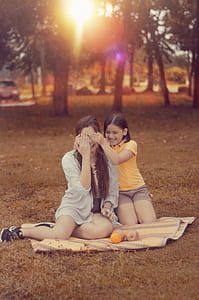 Two Women Sitting on Brown Picnic Mat during Sunset thumbnail