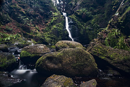 timelapse photo of waterfalls flowing between moss-covered stones and hills thumbnail