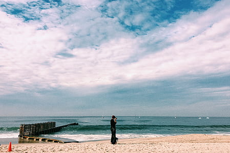Person in Black Top Standing on Seashore Under White Clouds thumbnail