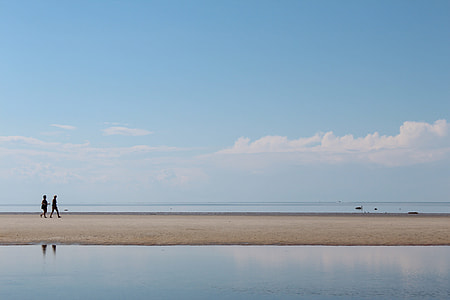 landscape photography of persons standing white sand near large body under cloudy sky during daytime thumbnail