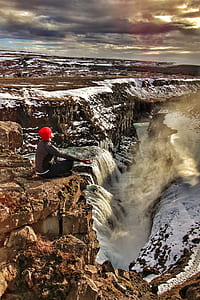 man sitting on top of cliff near waterfalls thumbnail