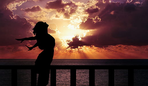 silhouette photography of woman with arms wide open beside calm body of water thumbnail