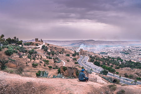 man sitting near road on hill during daytime thumbnail