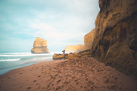 person on seashore in front of formation rock thumbnail