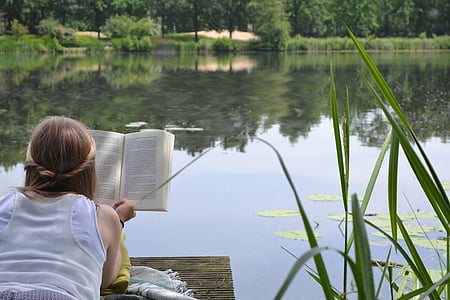 woman reading book on brown dock near lake thumbnail