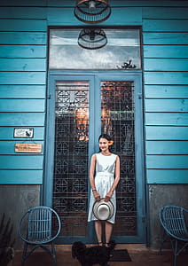 Woman Wearing Gray Satin Sleeveless Dress Holding Hat in Front of Door thumbnail