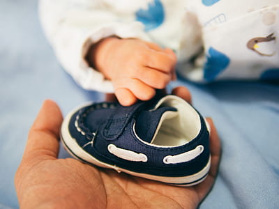 person holding baby shoe beside baby's hand thumbnail