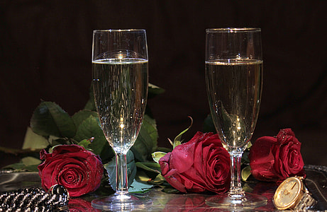 photo of two short-stemmed champagne flutes filled with liquid beside three red rose flowers thumbnail