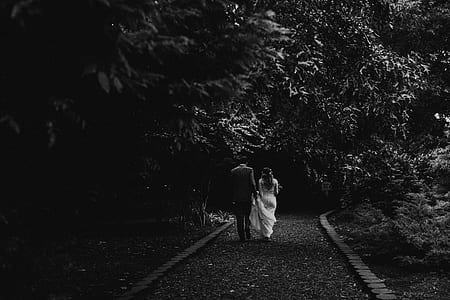 grayscale photo of couple walking between trees thumbnail