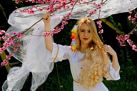 woman in white dress holding pink cherry blossom tree photo thumbnail