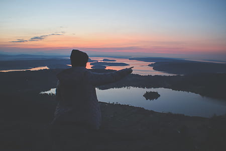 person sitting on cliff overlooking body of water during dusk thumbnail