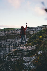 man in red hooded jacket standing on cliff thumbnail
