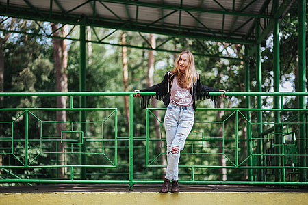 Blonde woman in a black jacket and ripped jeans by a green handrail thumbnail