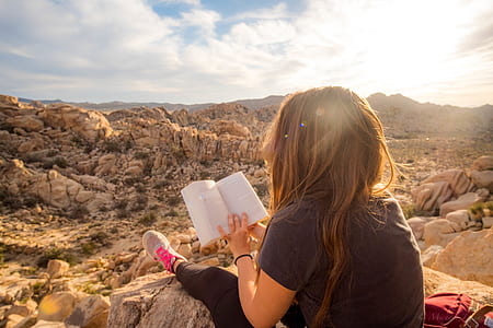 person reading book while sitting on rock thumbnail