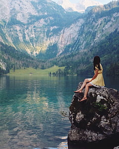 woman sitting on rock above body of water thumbnail