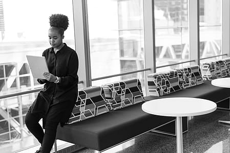 Grayscale Photo of Woman Holding Gray Notebook on Sofa Near Glass Window thumbnail