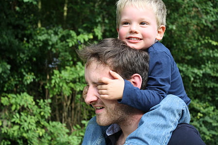 man piggy back ride smiling boy while covering his eyes during daytime thumbnail