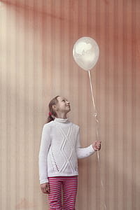 girl standing near wall holding on to balloon string thumbnail